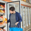 Man selecting frozen food from a Cold Room Refrigeration unit in a supermarket while carrying a blue shopping basket.